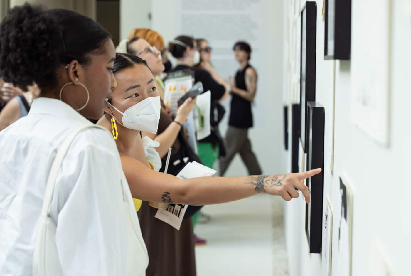 Visitors examine framed archival documents and photographs on a gallery wall, with one person pointing to a piece while others look on during a Chicago Poetry Center exhibition.